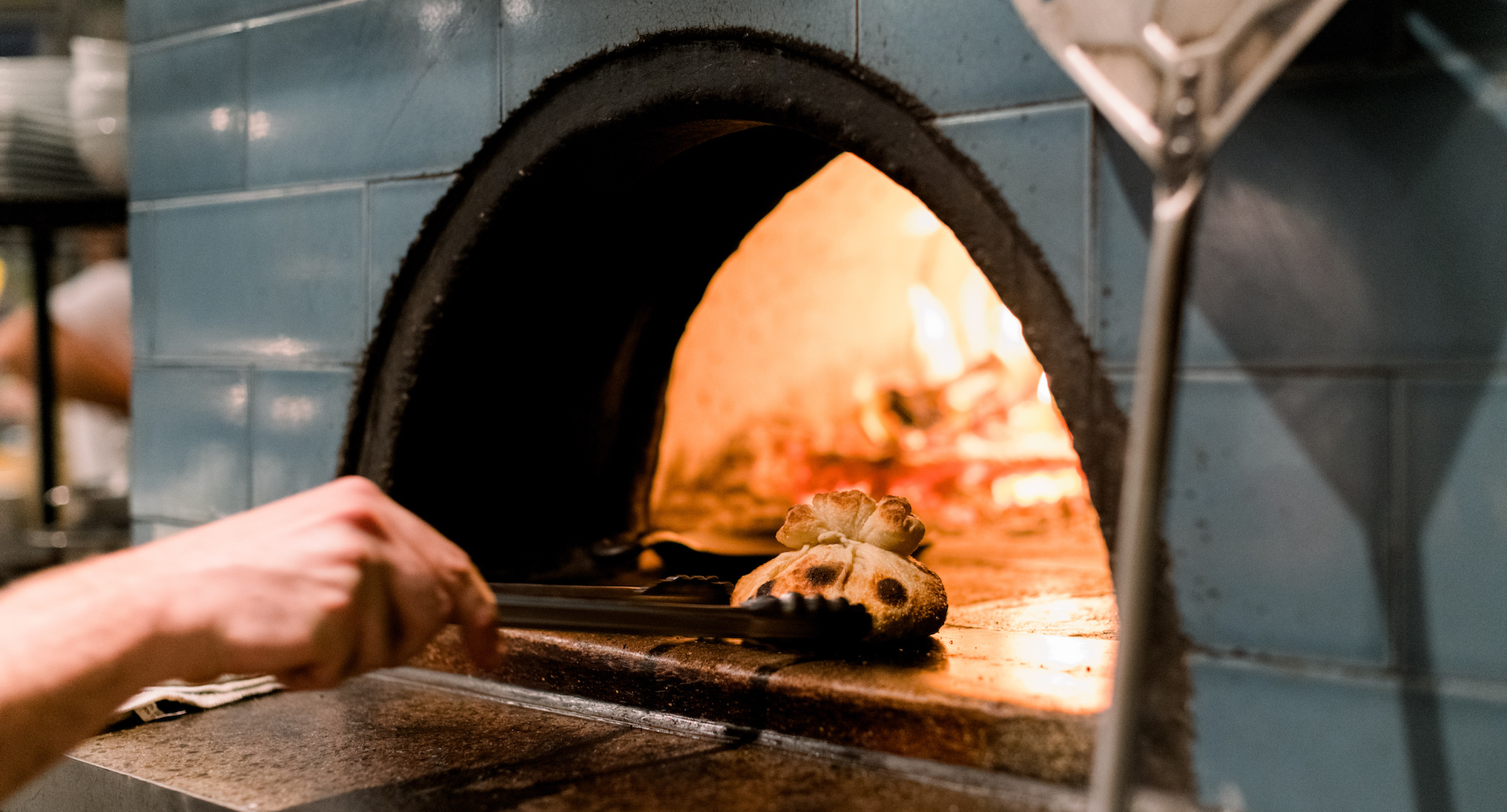 A hand moves a garlic knot in a wood fired oven