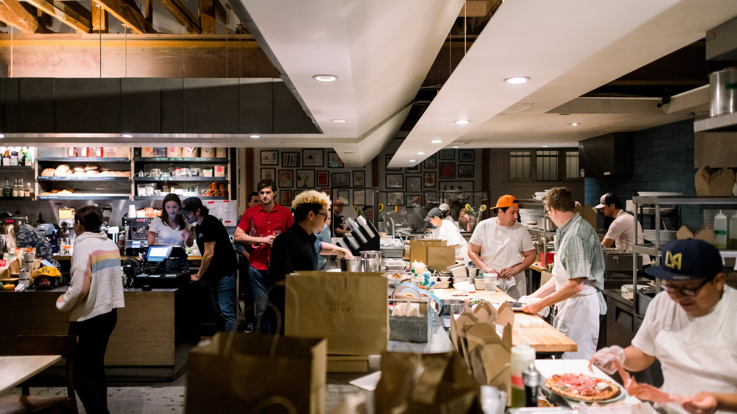 customers mingling, staff working and cooks topping pizzas